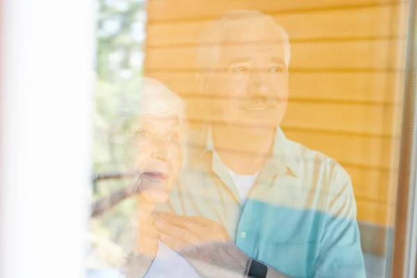Zeitgenössische Liebevolle Seniorengattinnen Stehen Fenster Ihres Landhauses Und Schauen Hindurch — Stockfoto