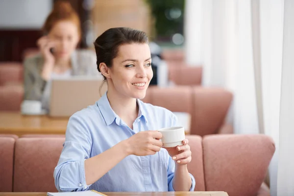 青いシャツを着た若いビジネスウーマンがテーブルに座り 窓を見ながらカフェでコーヒーを飲む — ストック写真