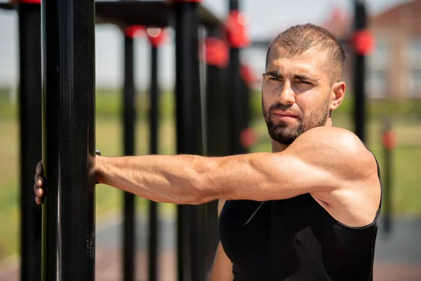 穿着黑色背心的肌肉男子在运动酒吧举行 同时在户外运动设施锻炼时伸展手臂 — 图库照片