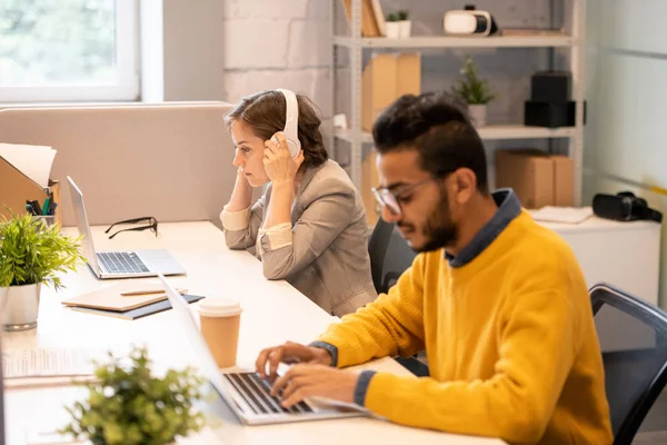 Serious busy multi-ethnic managers sitting at one table and using modern laptops while working with files in office