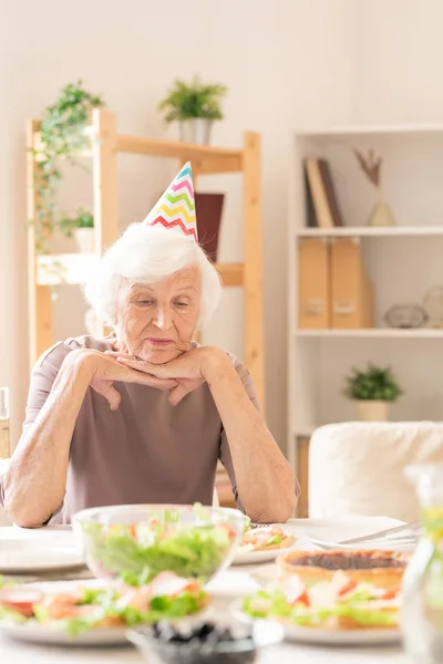 Triste Hembra Senior Gorra Cumpleaños Mirando Comida Casera Mientras Está — Foto de Stock