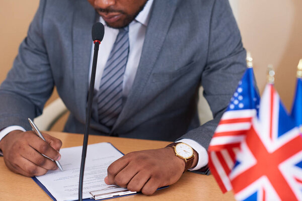 Young African-american elegant delegate making pointing at paper while reading it by table and preparing his speech