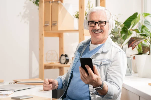 Erfolgreicher Alter Mann Kopfhörern Und Freizeitbekleidung Mit Smartphone Schreibtisch Vor — Stockfoto