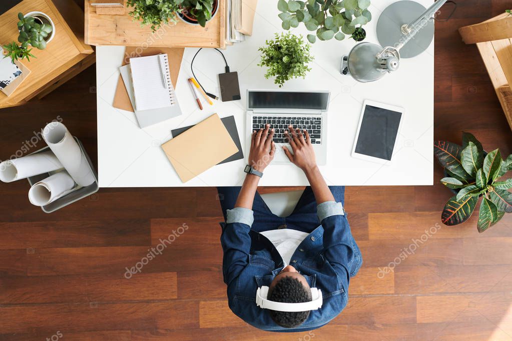 Contemporary casual guy with headphones looking at laptop display while typing on keypad on working day
