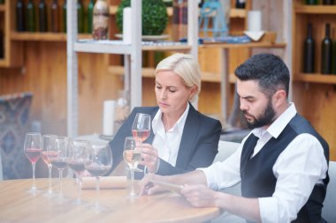 Şarap bardaklarında şarap örnekleri grubuyla masaya oturan ve ayrı ayrı çalışan iki ortak sommelier
