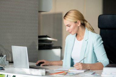 Genç ciddi tasarımcı işyeri tarafından online web siteleri üzerinden bakarken not defterine notlar yapma