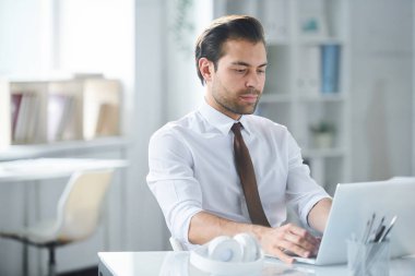 Ofisteki işyerinin dizüstü bilgisayar ekranına bakan formalgiyimli genç ciddi işadamı