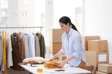 Genç yönetici paketleme için hazırlarken yeni mevsimlik casualwear koleksiyonu öğelerinden birini katlama