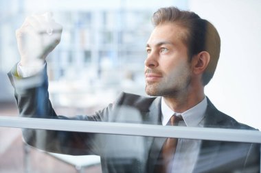 Antrenmanın puanlarını yazarken şeffaf tahtaya bakan formalgiyimli genç teknik direktör