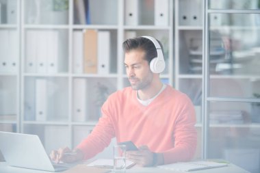 Ofiste çalışırken modern gadget'lar kullanarak kulaklık Casual genç işadamı