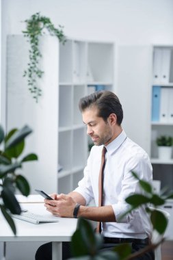 Akıllı telefonda müşterilerinin kişileri arasında gezinirken masa başında oturan formalgiyimgenç ajan