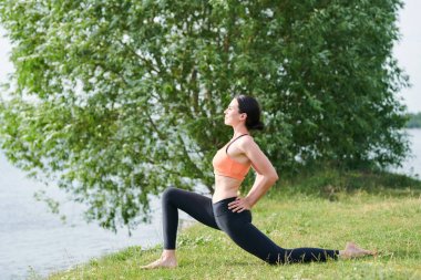Kıyıda yoga yaparken kalçalarında elleri ile düşük lunge poz yapıyor ince vücut ile güzel genç kadın