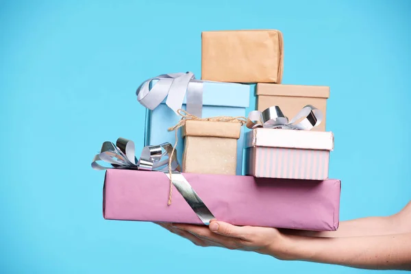 青い背景に孤立して女性の手が保持する箱にパックされ 包まれたプレゼントのスタック — ストック写真