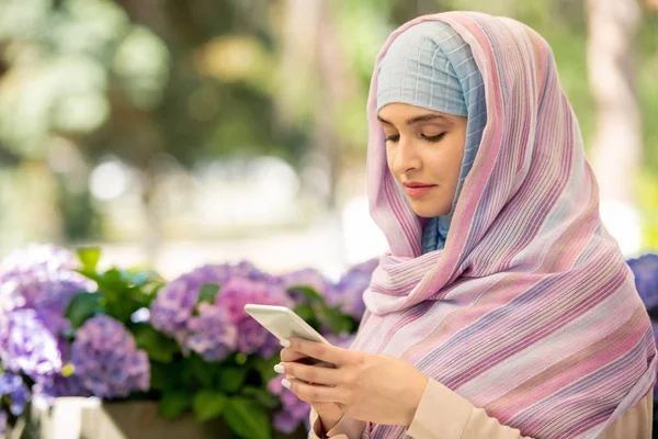 Wanita Arab Muda Mengenakan Jilbab Bergulir Smartphone Sambil Bersantai Taman — Stok Foto