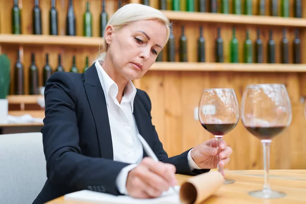 地下室での作業中に赤ワインの特性に関するメモを作るフォーマルウェアの経験豊富なワイナリーの専門家 — ストック写真