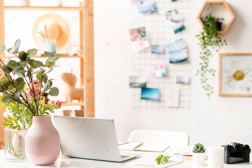 Workplace of designer of interior with laptop, office supplies and floral compositions on desk