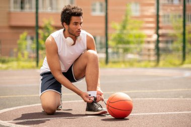 Genç profesyonel basketbolcu sahada oyun için hazırlanırken spor ayakkabı ayakkabı bağcık bağlama