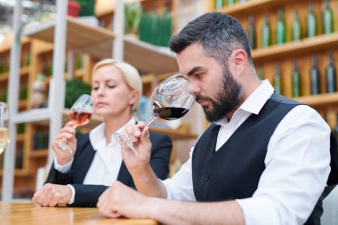 Kalitesini incelerken şarap kadehinde kırmızı şarap yeni tür kokulu formalwear genç sakallı sommelier