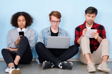 Proje veya ev ödevi üzerinde tek tek çalışan gadget'lar ve dizüstü bilgisayar ile thrre genç yaratıcı grup arkadaşları