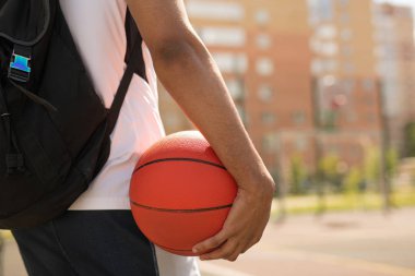 Açık hava antrenmanı öncesi oyun alanında duran top ve sırt çantası ile genç basketbolcu