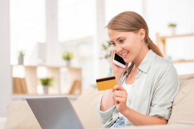 Plastik kart ve akıllı telefon ile Çağdaş kız dizüstü bilgisayar önünde online alışveriş yöneticisi konuşuyor