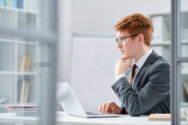 Dizüstü bilgisayar önünde entelektüel çalışma üzerine yoğunlaşan formalwear genç ciddi analist