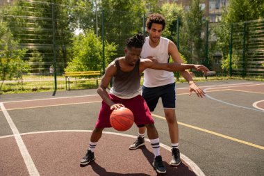 Genç profesyonel basketbolcu sahada oyun sırasında rakibin saldırısından topu savunan
