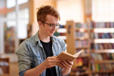Seminer öncesi kütüphanede denim gömlek ve siyah tee okuma kitabı genç üniversite öğrencisi