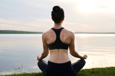 Çim üzerinde çapraz bacaklar ile oturan ve gün batımında meditasyon siyah spor genç kadın arka görünümü
