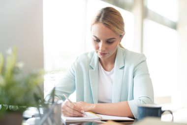 Masa başında otururken not alma veya not defterine çizim yapan akıllı ve yaratıcı öğrenci