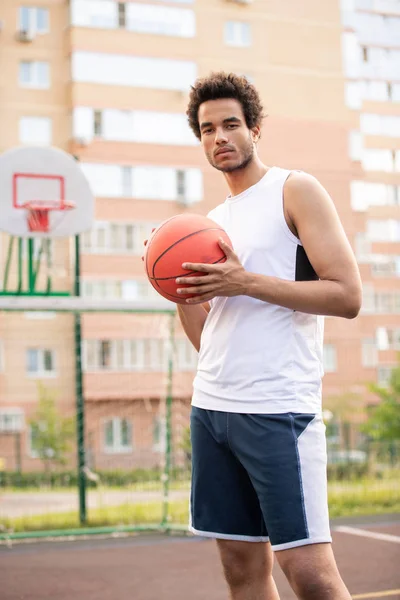 Young athlete in white t-shirt and sports shorts holding ball for playing basketball while standing on the court