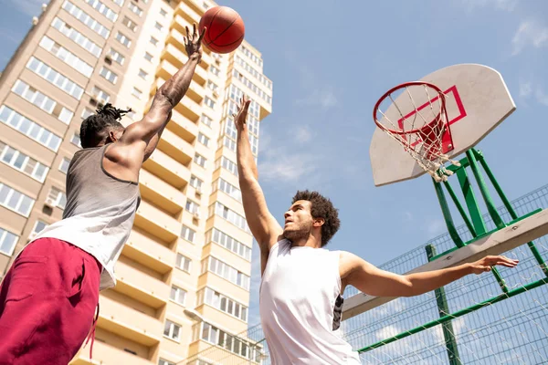 ボールをキャッチしようとするアクティブウェアの2人の若いプロの異文化バスケットボール選手 — ストック写真