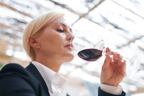 その匂いを評価しながら 彼女の鼻で赤ワインのボカルを保持する深刻な成熟したワイナリーの専門家 — ストック写真
