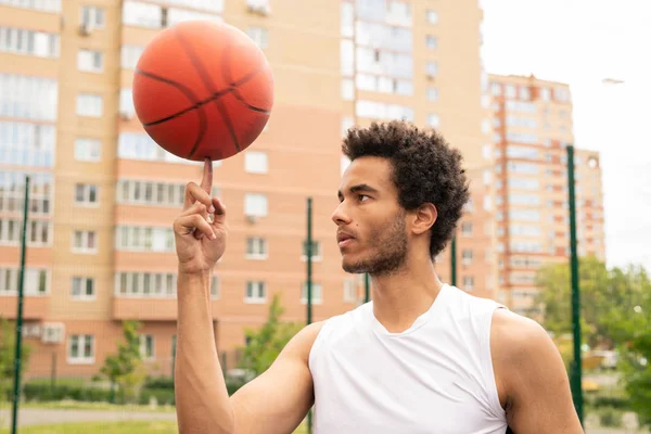 若いアクティブなプロバスケットボール選手は それを見ながら人差し指に回転ボールを保持 — ストック写真
