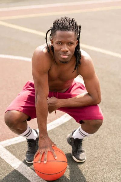 Jonge Gespierde Atleet Met Bal Zittend Squats Voor Camera Speelplaats — Stockfoto