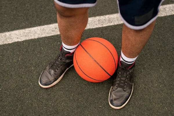 白線で遊び場に立つ若いプロバスケットボール選手の足によるボール — ストック写真