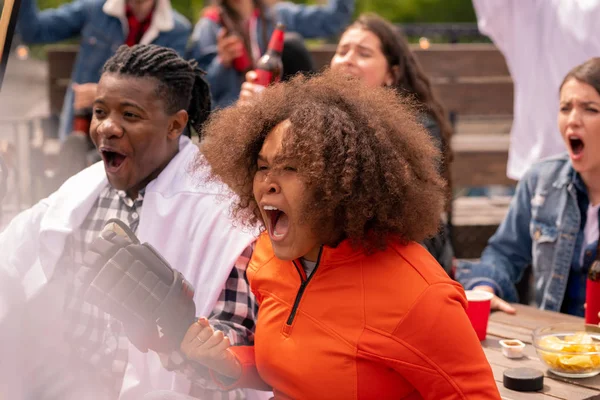 Young multicultural emotional couple of hockey fans cheering for their favorite team during broadcast of match