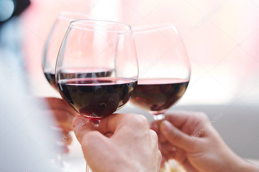 Three wineglasses with red cabernet held by toasting friends enjoying party and celebrating holiday