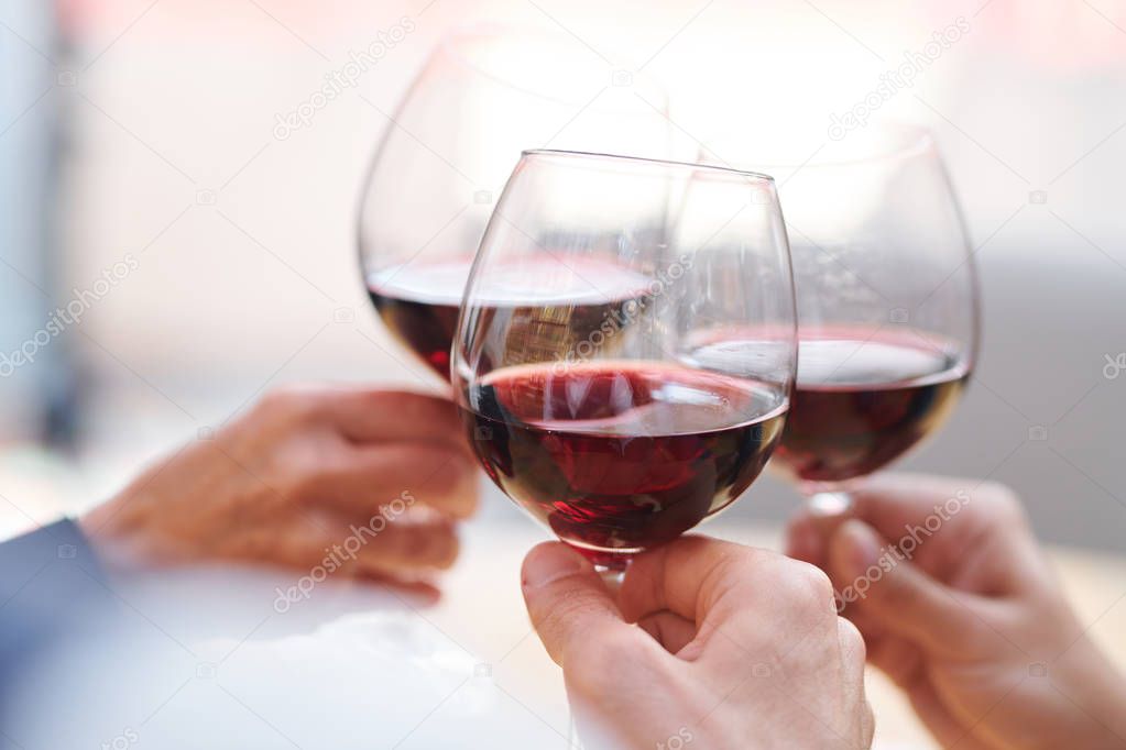 Three wineglasses with red cabernet held by group of friends clinking while congratulating one another on holiday