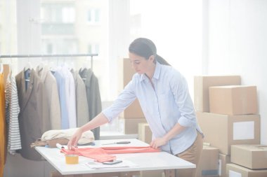Online mağaza genç ofis yöneticisi paketleme den önce katlanırken müşterilerinden biri için casualwear hazırlanıyor