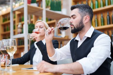 Genç erkek sommelier arka planda onun coleague tatma içecek ile bokal kırmızı şarap kokulu