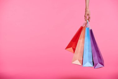 Renkli kağıt torbalar demet tutan veya pembe arka plan üzerinde alışveriş yaptıktan sonra onları taşıyan alışveriş el