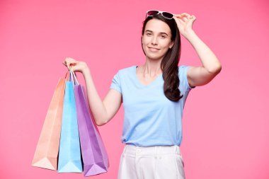 Pembe arka planda izole kamera önünde duran t-shirt, pantolon ve güneş gözlüğü Pretty alışveriş