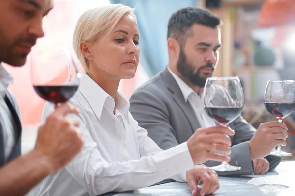 严肃的金发女郎看着红酒在博卡 同时评估她的同事之间的饮料的颜色 — 图库照片