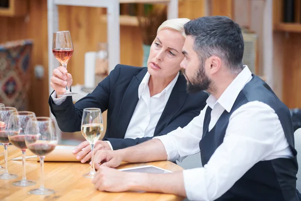 Pretty sommelier with glass of white wine giving its chracteristics in conversation with colleague