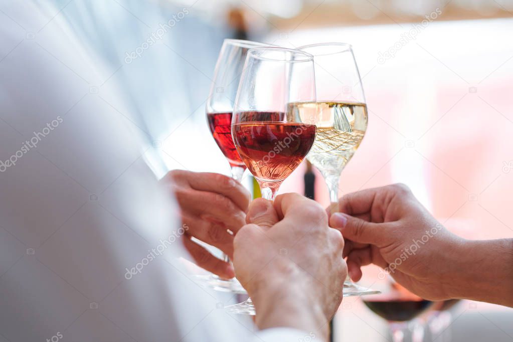 Human hands holding wineglasses with champagne, cabernet and brandy while clinking during toast