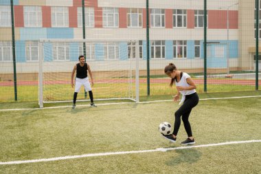 Arka planda sporcu ile oynamayı öğrenirken futbol sahasında duran spor giyim genç kadın