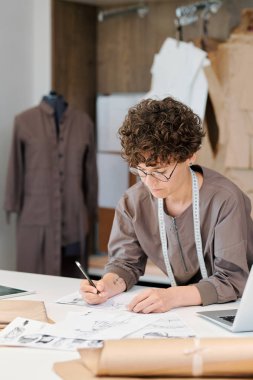 Koleksiyon için yeni moda modellerinin skeçler yaparken masa üzerinde bükme genç esmer kadın