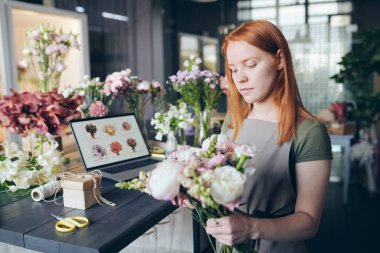 Çiçek ve dekorasyon araçları dolu sayaç tarafından ayakta önlük meşgul çekici kız ve çiçek mağazasında çalışırken buket çiçek karıştırma