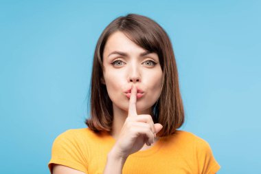 Young pretty brunette female keeping forefinger by her pouted lips while asking to be quiet clipart